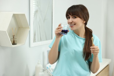 Photo of Young woman using mouthwash in bathroom. Oral hygiene