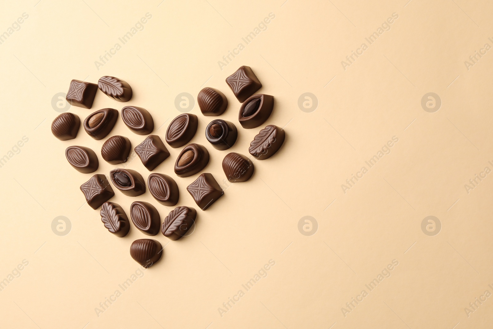 Photo of Heart made with delicious chocolate candies on beige background, above view. Space for text