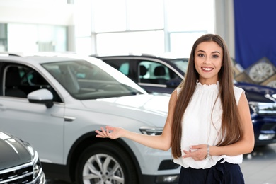 Young saleswoman standing in modern car salon