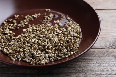 Photo of Plate of gold nuggets on wooden table, closeup