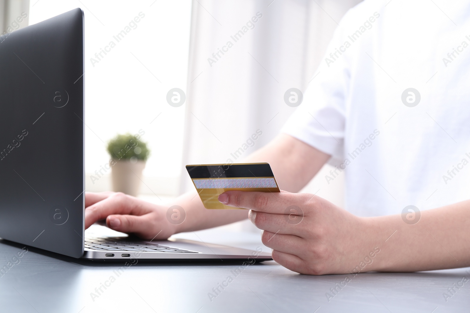 Photo of Online payment. Woman with laptop and credit card at white table, closeup