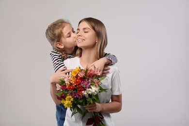 Little daughter congratulating her mom with flowers on white background. Happy Mother's Day