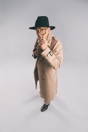 Male detective with smoking pipe looking through magnifying glass on grey background