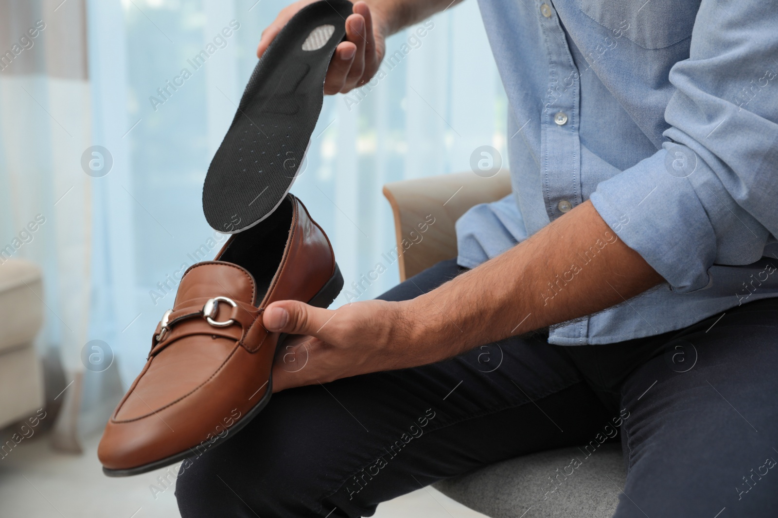 Photo of Man putting orthopedic insole into shoe indoors, closeup. Foot care