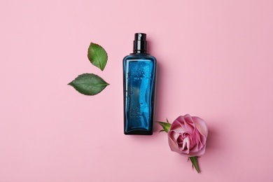 Photo of Bottle of perfume and rose on color background, top view