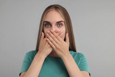 Photo of Embarrassed woman covering mouth with hands on grey background