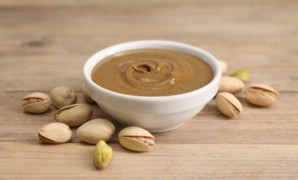 Delicious nut butter in bowl and pistachios on wooden table