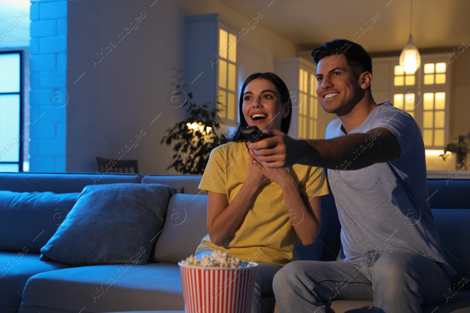 Photo of Couple watching movie with popcorn on sofa at night, space for text