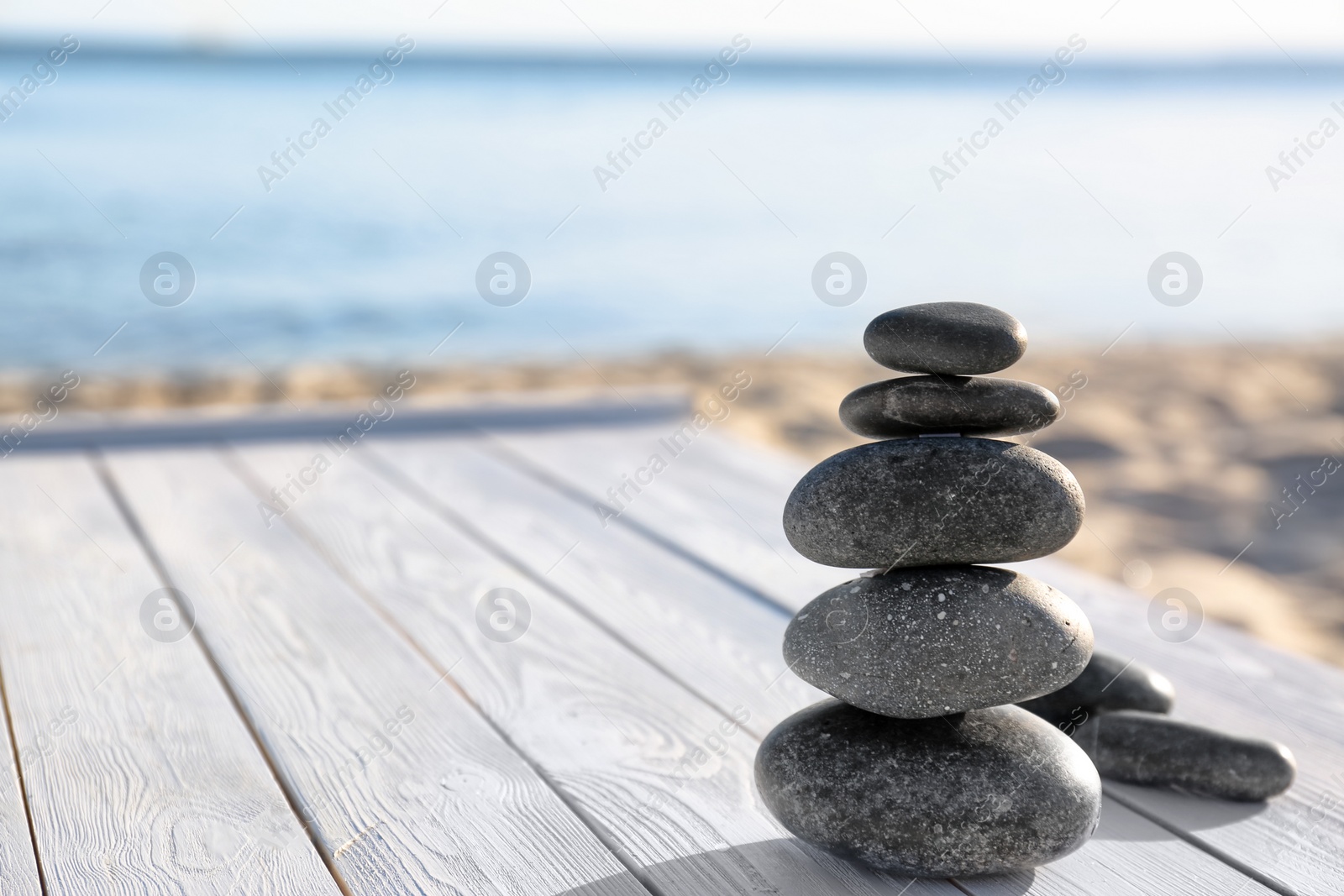 Photo of Stack of dark stones on wooden deck near sea, space for text. Zen concept