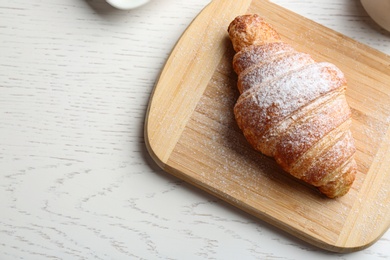 Photo of Board with tasty croissant, powdered sugar and space for text on white wooden table, above view. French pastry