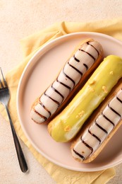 Different tasty glazed eclairs served on color textured table, top view