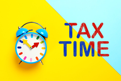 Time to pay taxes. Alarm clock on color background, top view