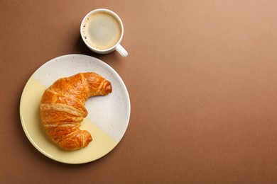 Delicious fresh croissant and cup of coffee on brown table, flat lay. Space for text