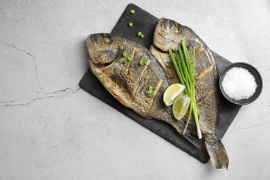Photo of Seafood. Delicious baked fish served with green onion and lime on light textured table, top view. Space for text