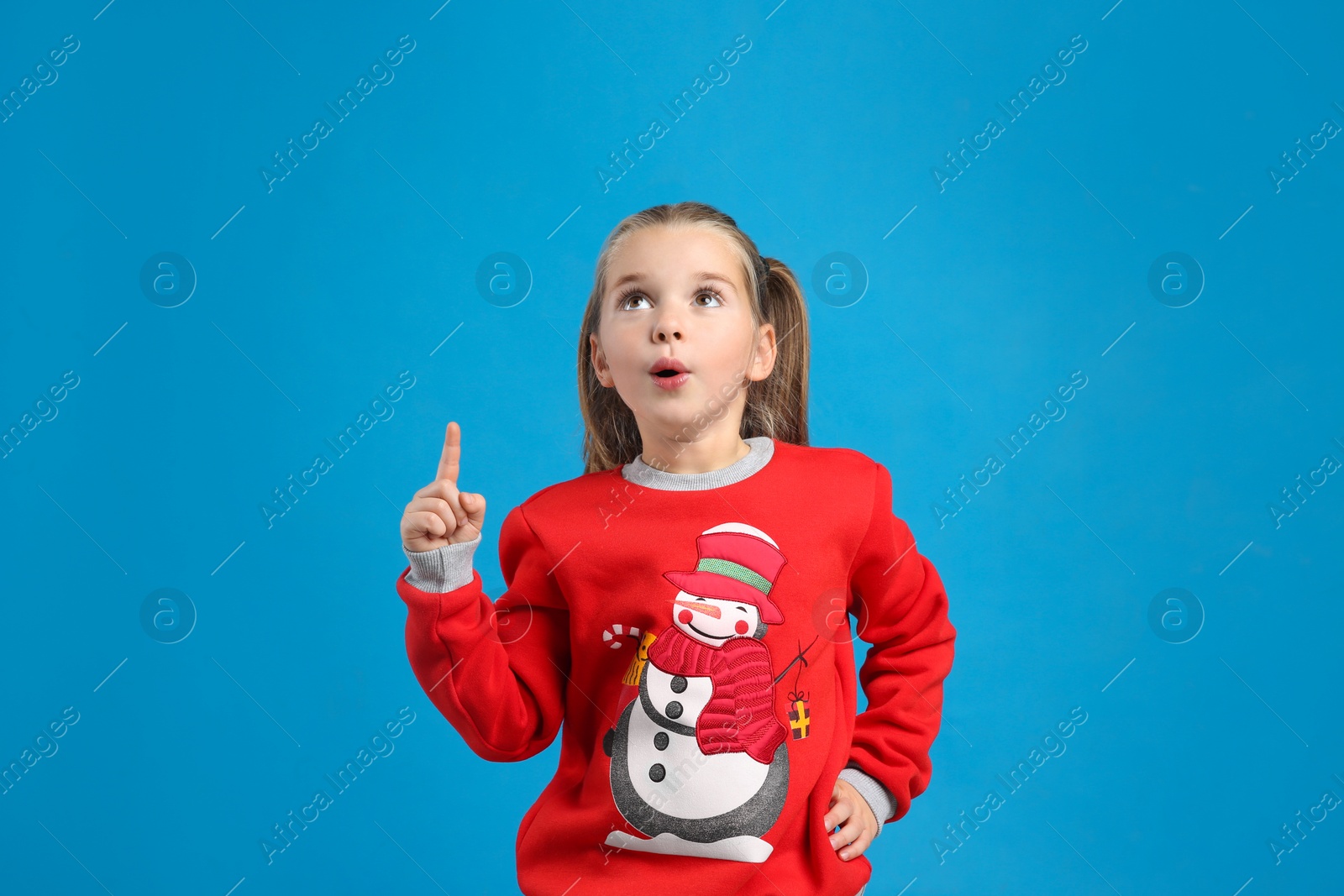 Photo of Surprised little girl in Christmas sweater on blue background