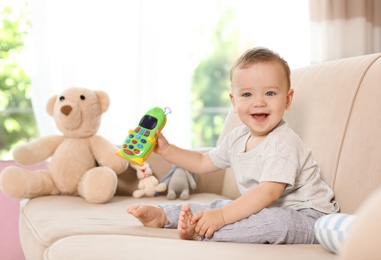 Photo of Adorable little baby with toy phone on sofa at home