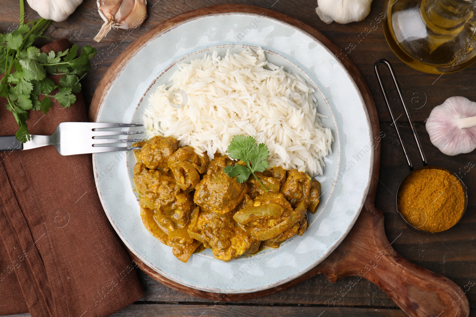 Photo of Delicious chicken curry with rice and ingredients on wooden table, flat lay