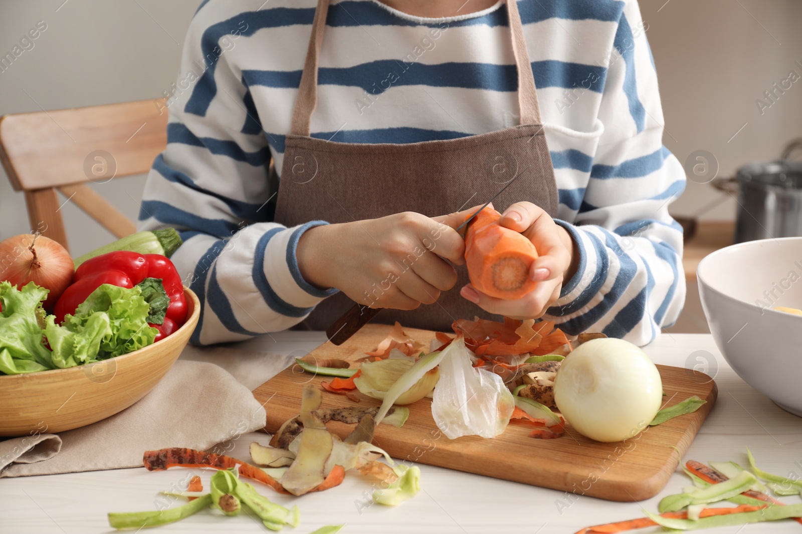 Photo of Woman peeling fresh carrot with knife at white table indoors, closeup