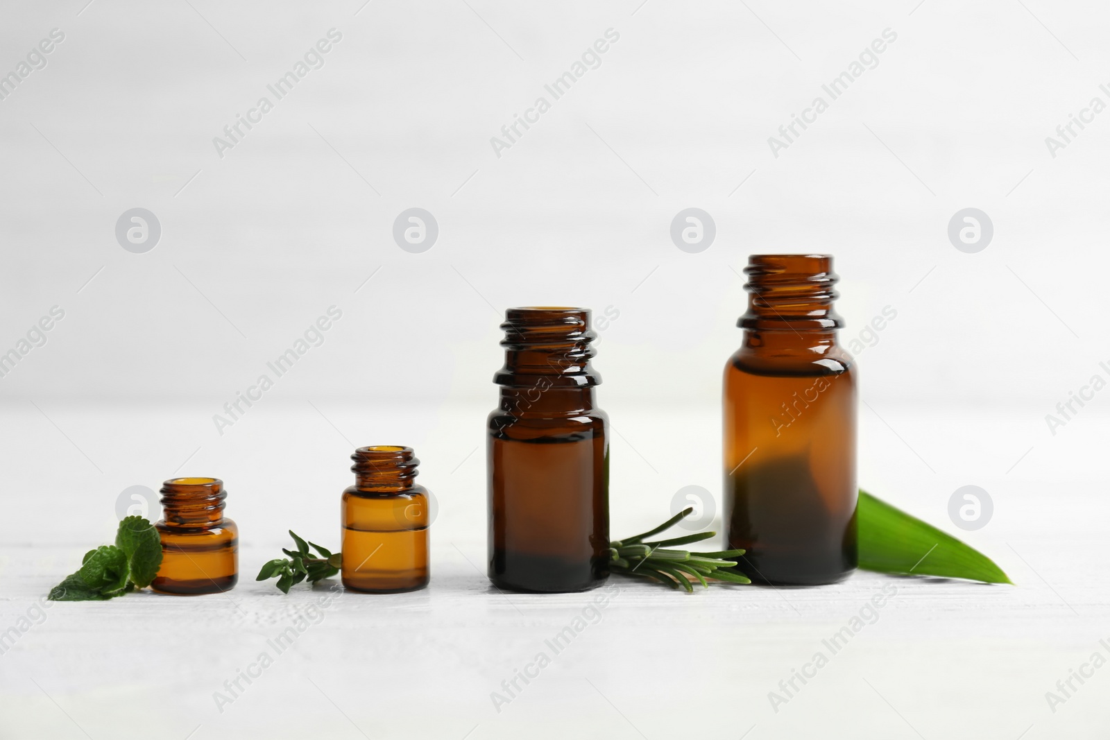 Photo of Bottles with essential oils and fresh herbs on light background