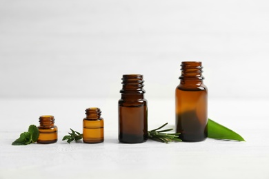 Photo of Bottles with essential oils and fresh herbs on light background