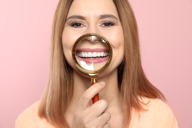 Smiling woman with perfect teeth and magnifier on color background, closeup