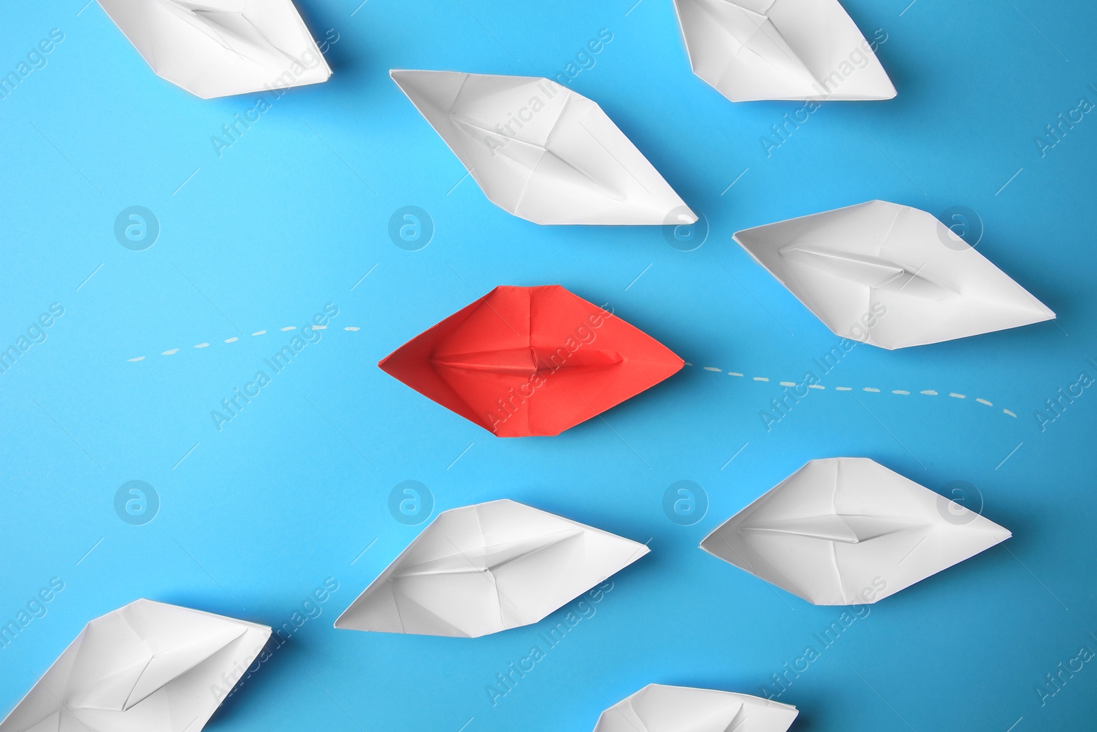 Photo of Red paper boat floating between others on light blue background, flat lay. Uniqueness concept