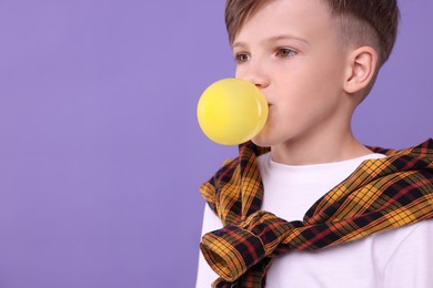 Boy blowing bubble gum on purple background, space for text