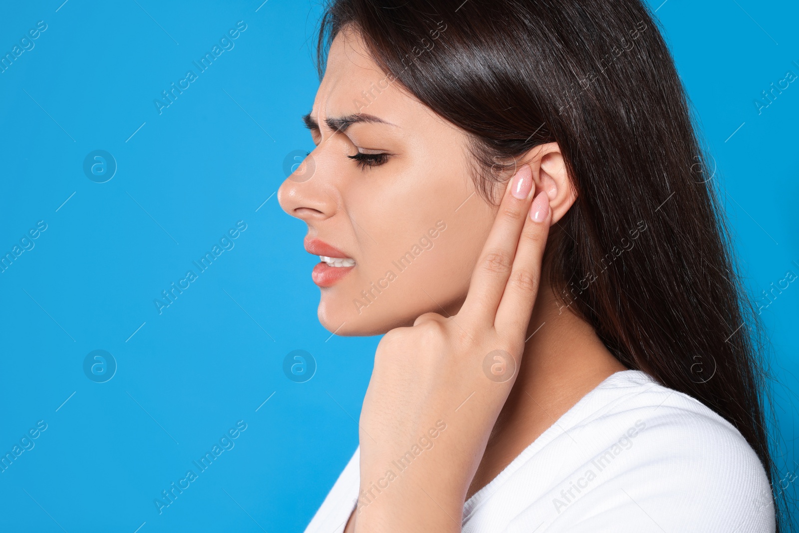 Photo of Young woman suffering from ear pain on light blue background, closeup. Space for text