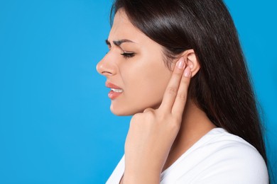 Photo of Young woman suffering from ear pain on light blue background, closeup. Space for text