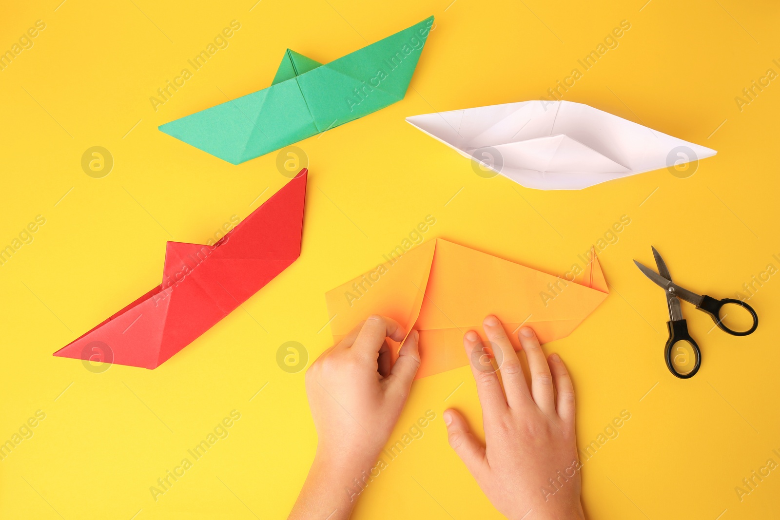 Photo of Origami art. Child folding paper on yellow background, closeup and top view
