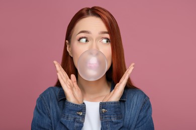 Photo of Surprised woman blowing bubble gum on pink background