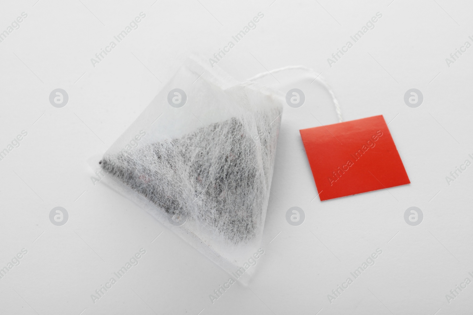 Photo of Unused pyramid tea bag with tag on white background. Space for text