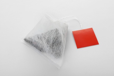 Photo of Unused pyramid tea bag with tag on white background. Space for text