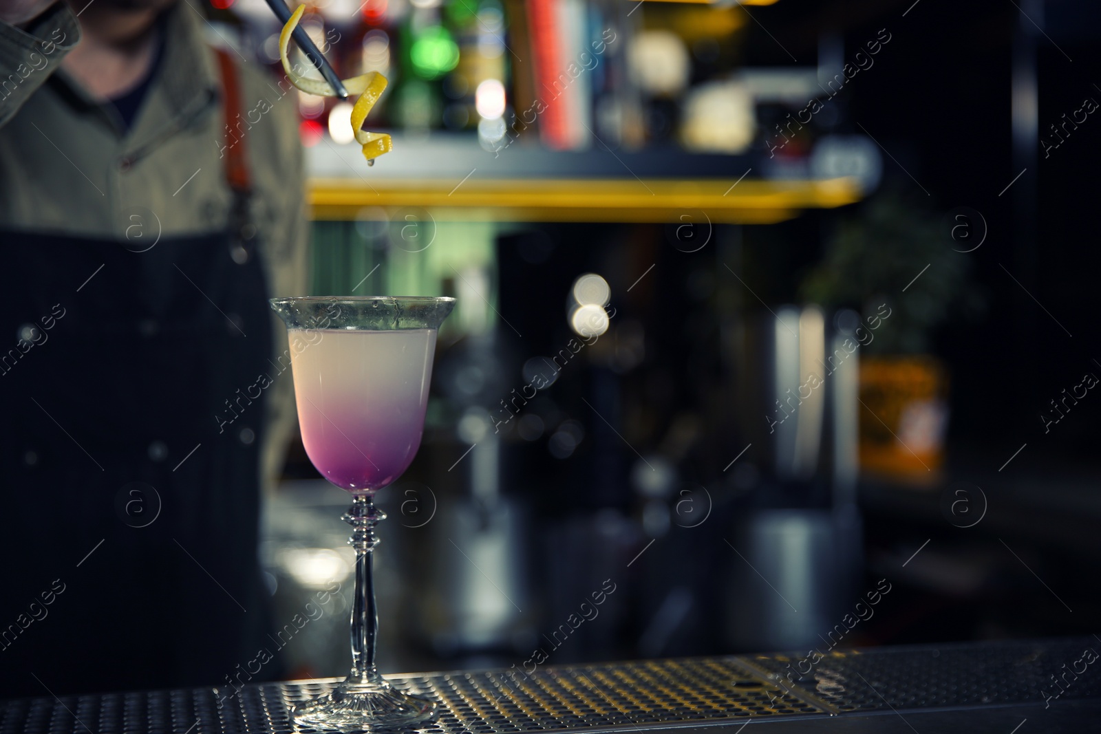 Photo of Barman adding lemon zest into cosmopolitan martini cocktail at counter, closeup. Space for text