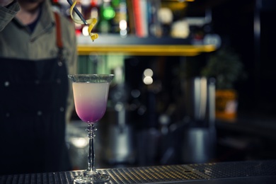 Photo of Barman adding lemon zest into cosmopolitan martini cocktail at counter, closeup. Space for text