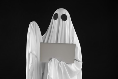 Photo of Creepy ghost. Person in white sheet with laptop on black background
