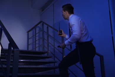 Male security guard with flashlight and portable radio transmitter in dark room