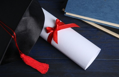 Photo of Graduation hat, books and student's diploma on dark blue wooden table, above view