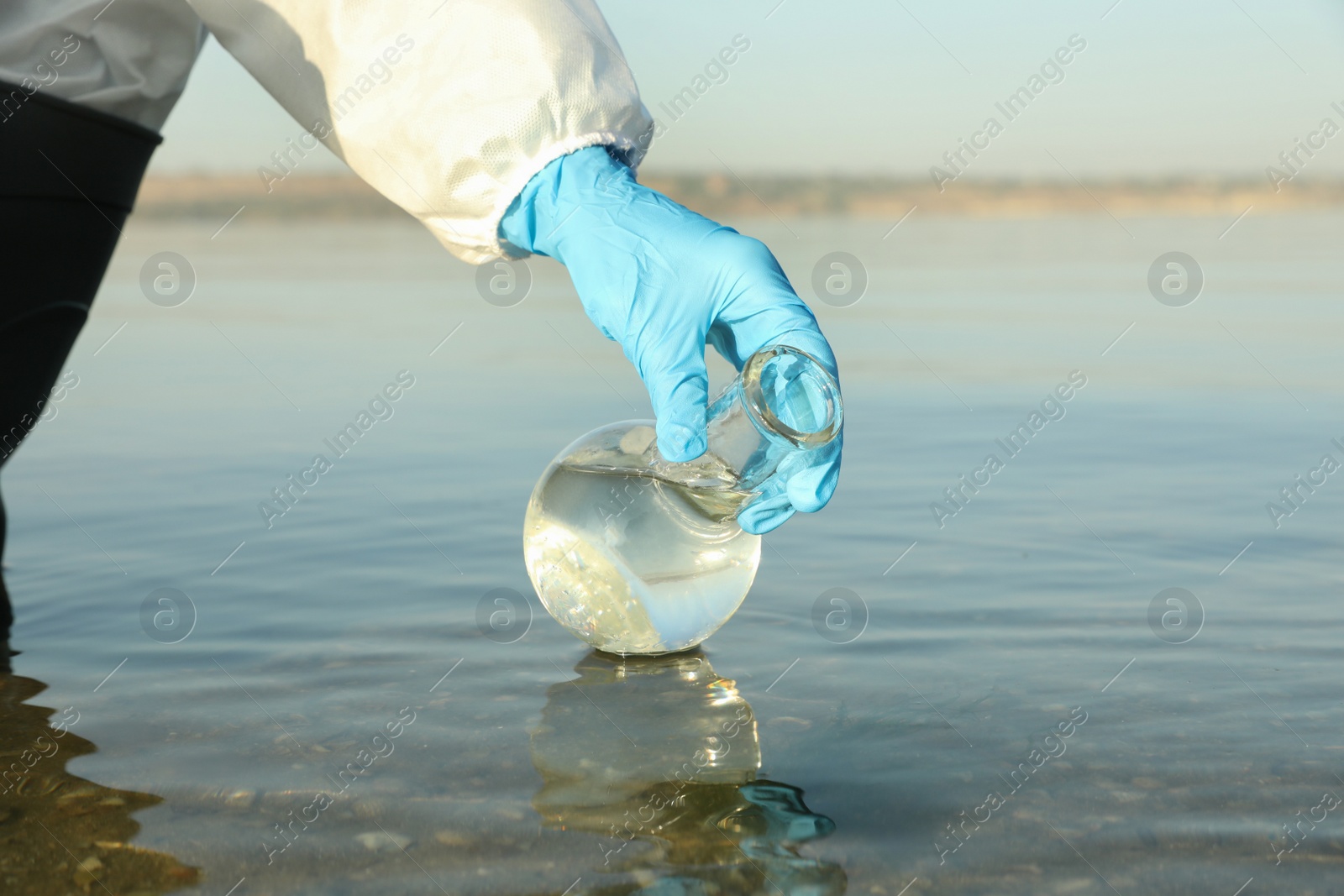 Photo of Scientist with florence flask taking sample from river for analysis, closeup