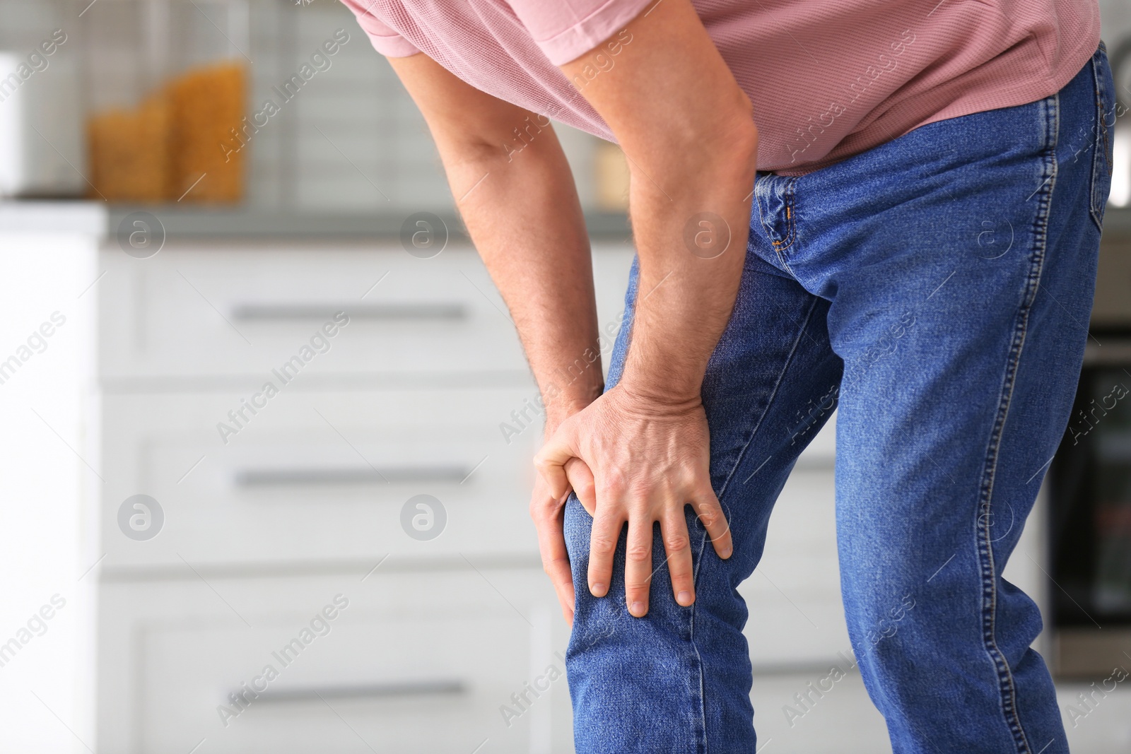 Photo of Senior man suffering from knee pain in kitchen, closeup. Space for text