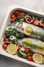 Photo of Raw fish with vegetables and lemon in baking dish on grey textured table, top view