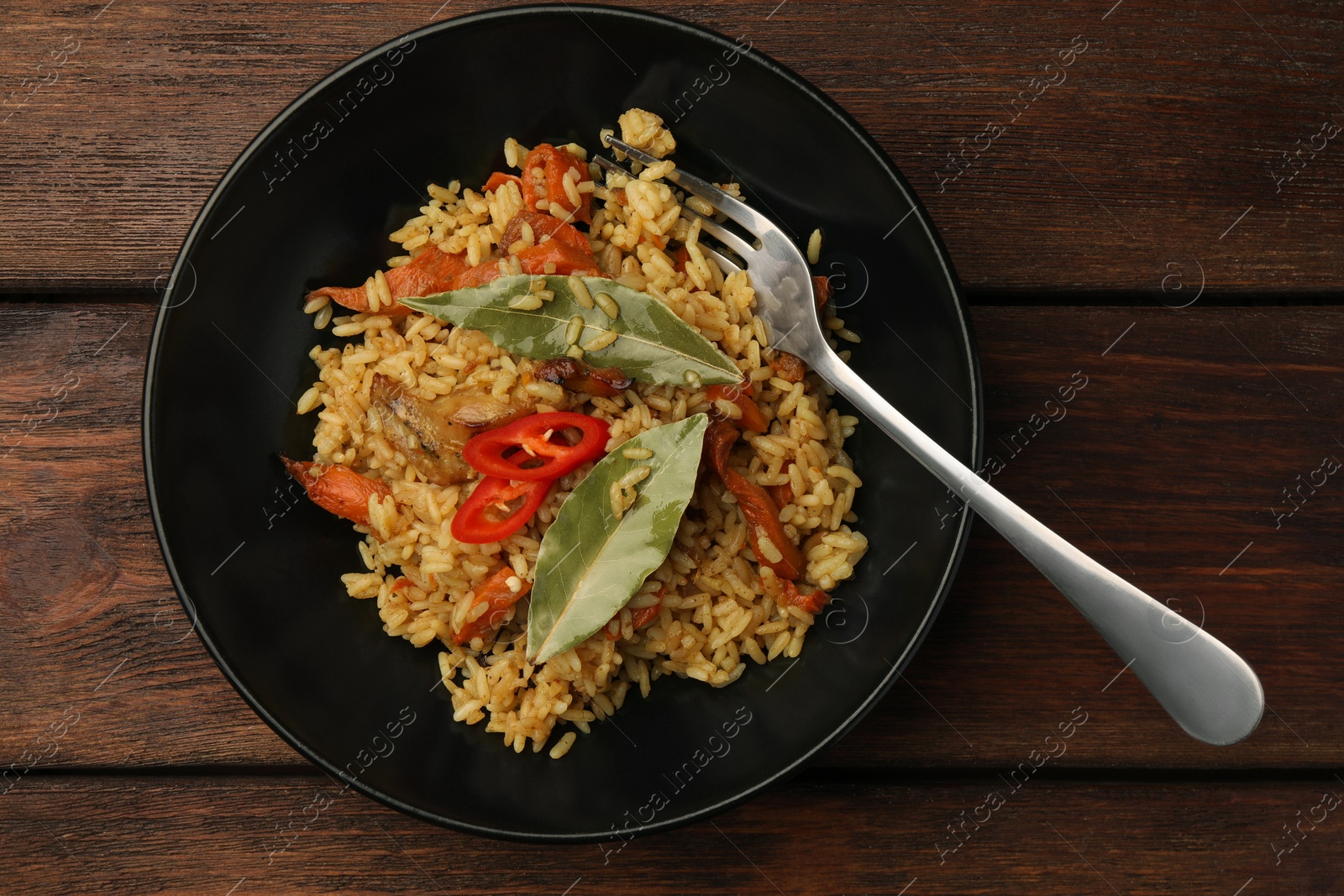 Photo of Delicious pilaf, bay leaves and fork on wooden table, top view
