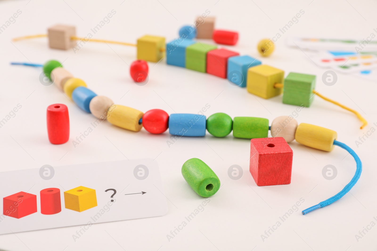 Photo of Wooden pieces and string for threading activity on white table. Motor skills development