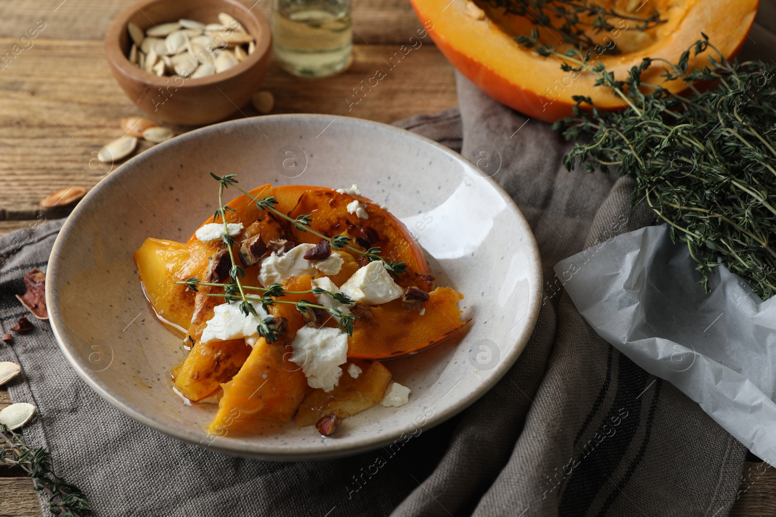 Photo of Baked pumpkin slices served with cheese, thyme and pecans on wooden table, closeup