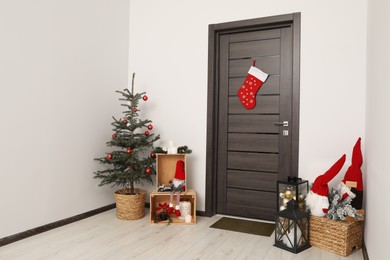 Photo of Christmas stocking hanging on wooden door and festive decoration indoors