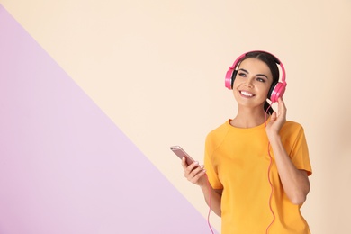 Photo of Attractive woman with mobile phone enjoying music in headphones on color background. Space for text