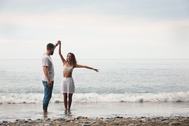 Photo of Happy young couple dancing on beach near sea. Space for text