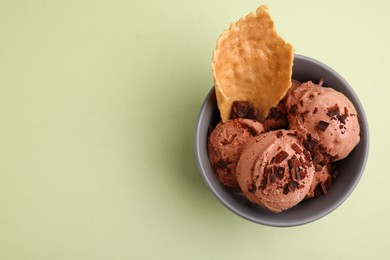 Tasty chocolate ice cream and piece of waffle cone in bowl on light green background, top view. Space for text