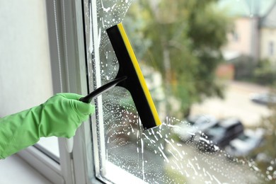 Photo of Woman cleaning glass with squeegee indoors, closeup