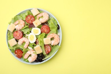 Delicious Caesar salad with shrimps on yellow background, top view. Space for text